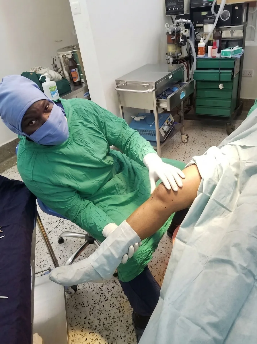 Dr. Raymond Joseph Malinga examining a patient with a knee X-ray displayed
